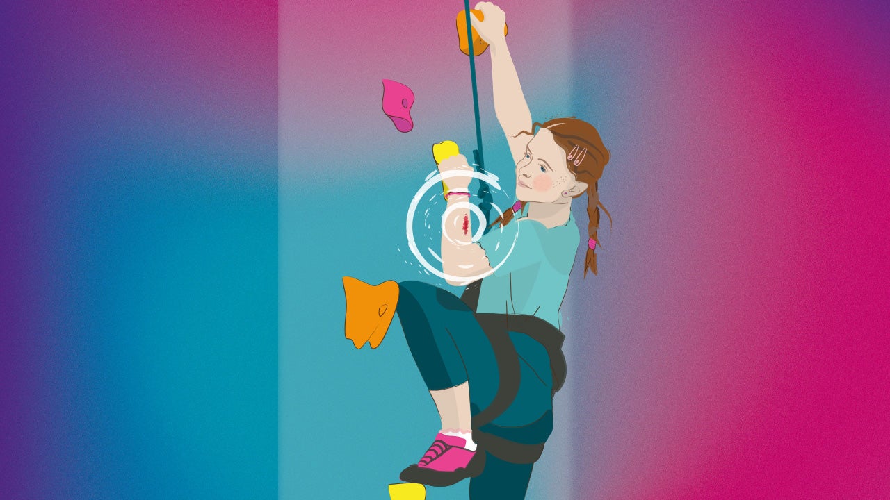 Kind klettert gesichert eine Kletterwand nach oben, am Arm ist eine Verletzung zu sehen